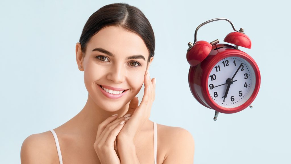 Mujer sonriente junto a un reloj despertador, simbolizando la importancia del tiempo en la vitrificación y congelación de gametos y embriones.